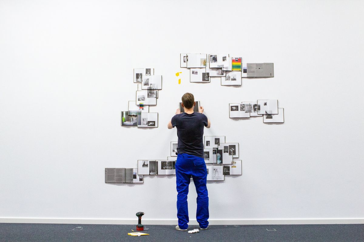artist Peter Puklus installing a total of 35 copies of his book "Handbook to the Stars" on a wall in the Wilhelm Hack Museum in Ludwigshafen for the exhibition of the Biennale für aktuelle Fotografie 2020